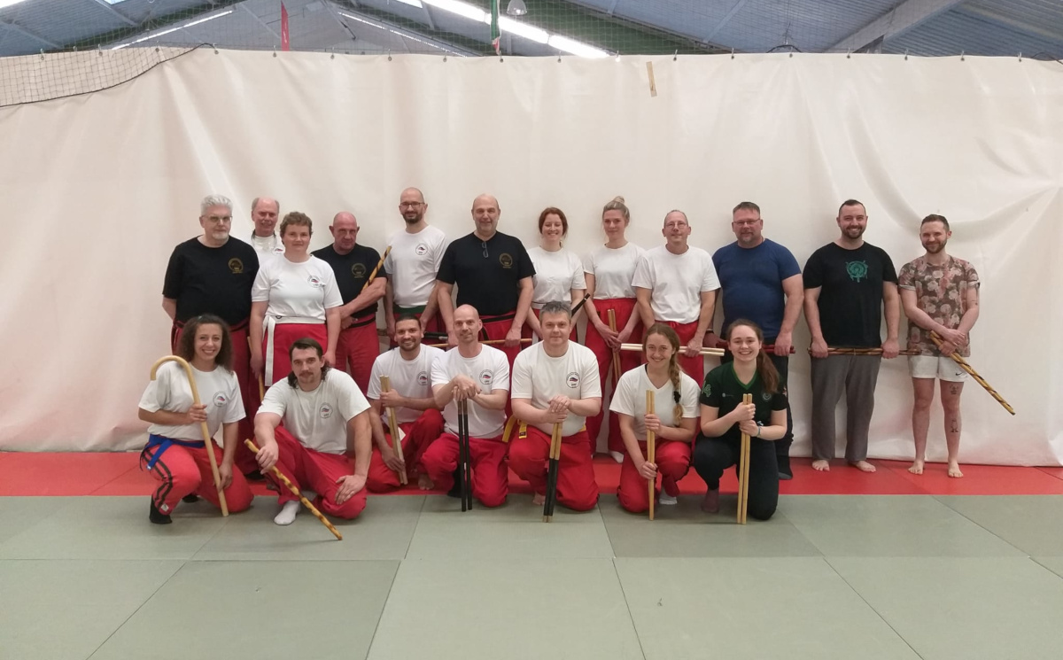 Gemischtes Gruppenfoto mit Modern Arnis-Sportbetreibenden mit Stöckern, roten Hosen und weißen T-Shirts. 